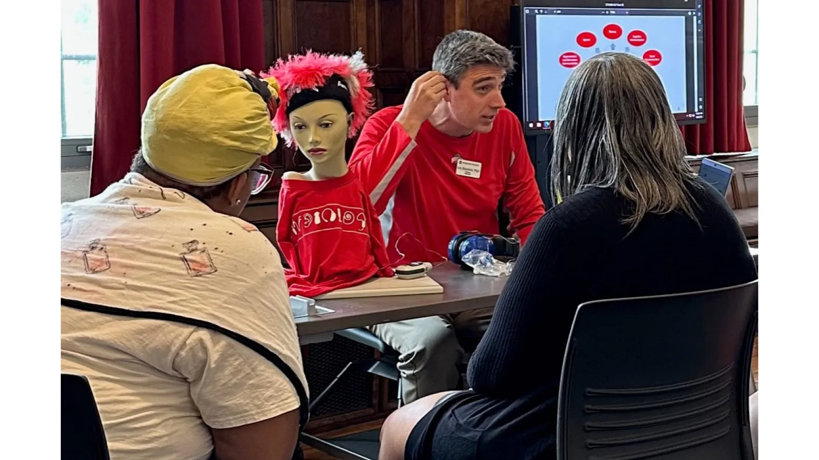 Eric Bielefeld demonstrating hearing aids for 2 participants