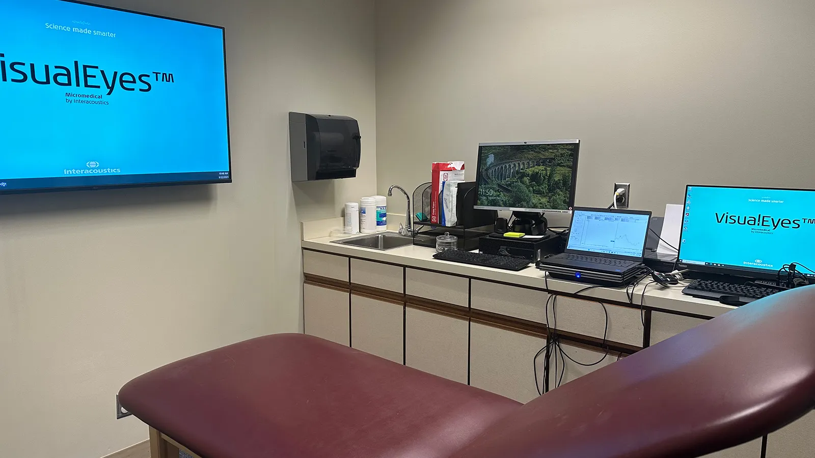 Clinic room with patient chair, computers, and TV screen