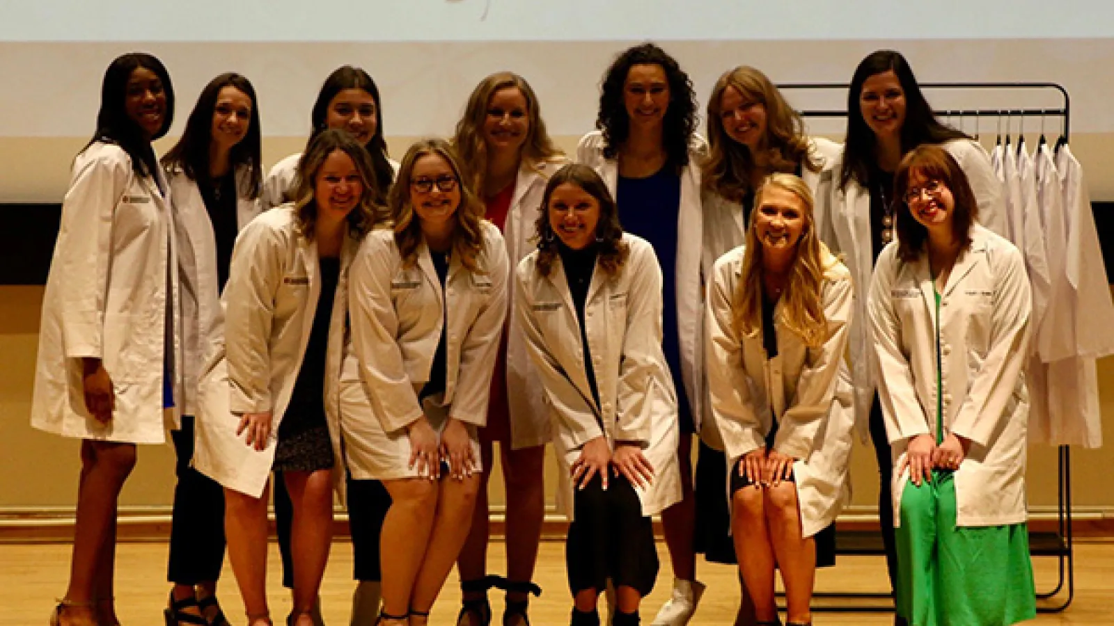 12 AuD students posing in white coats at ceremony