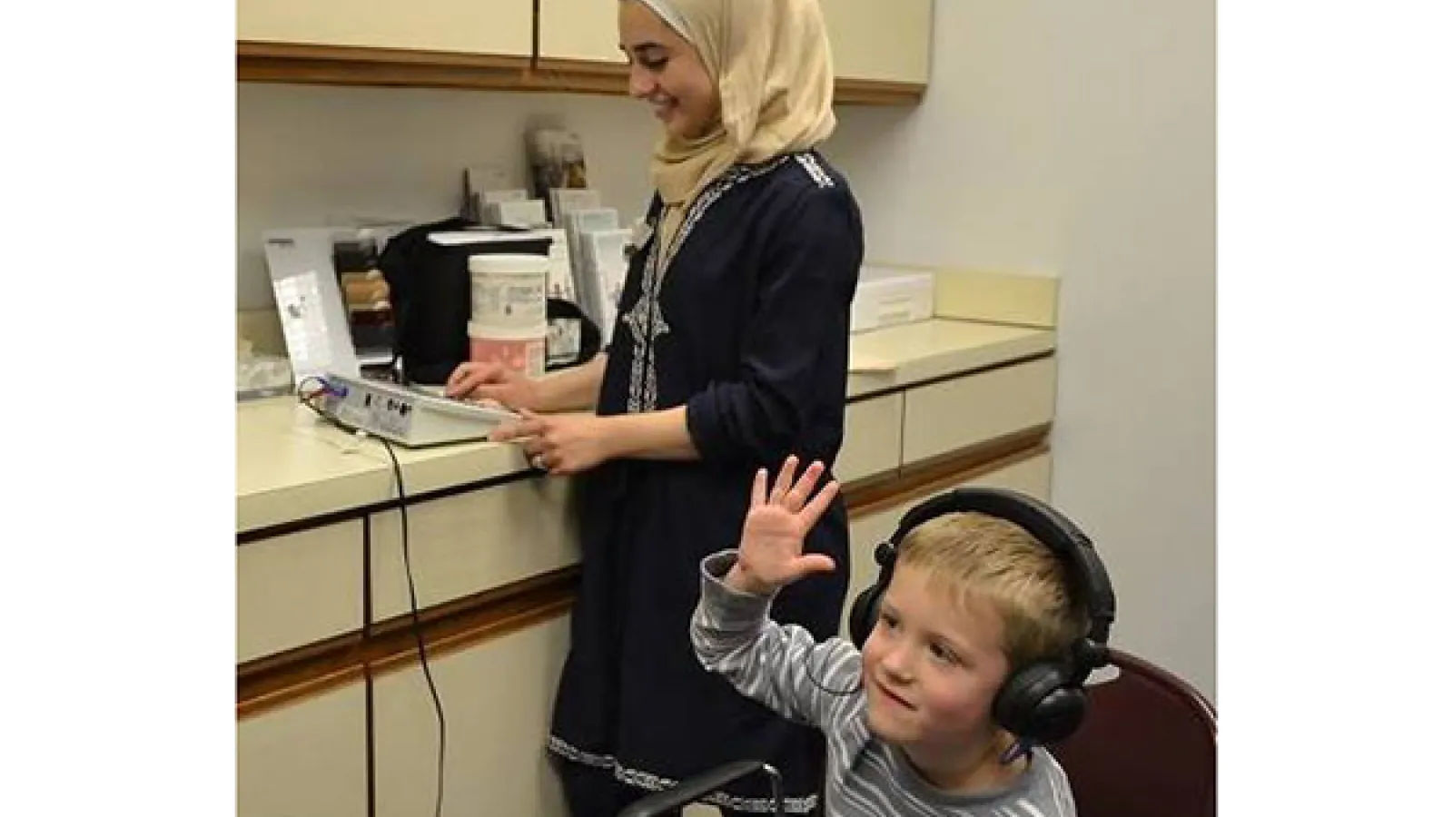 Child with headphones raising hand while student clinician administers hearing test