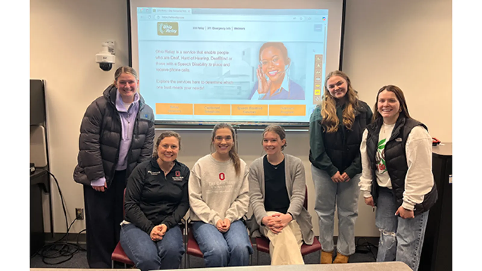 Group photo of students and instructor posing in front of presentation screen