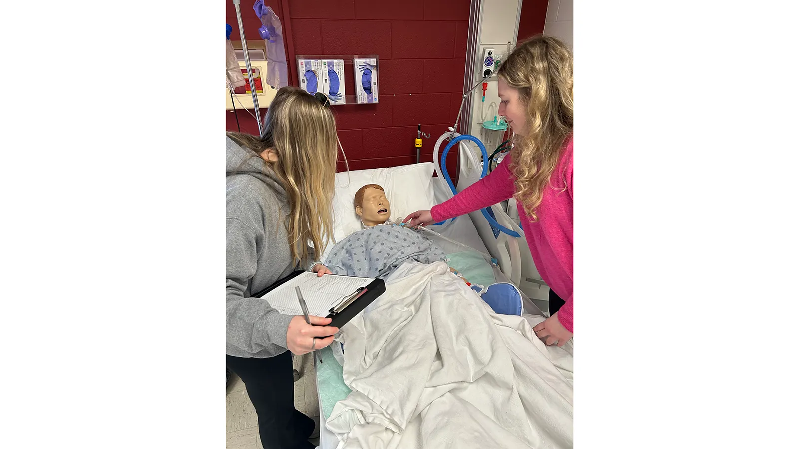 Two students on either side of hospital bed with mannequin