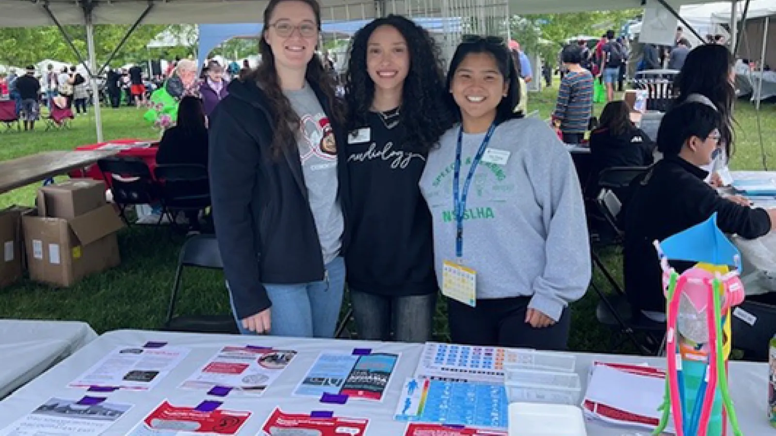3 students at table under a tent at festival