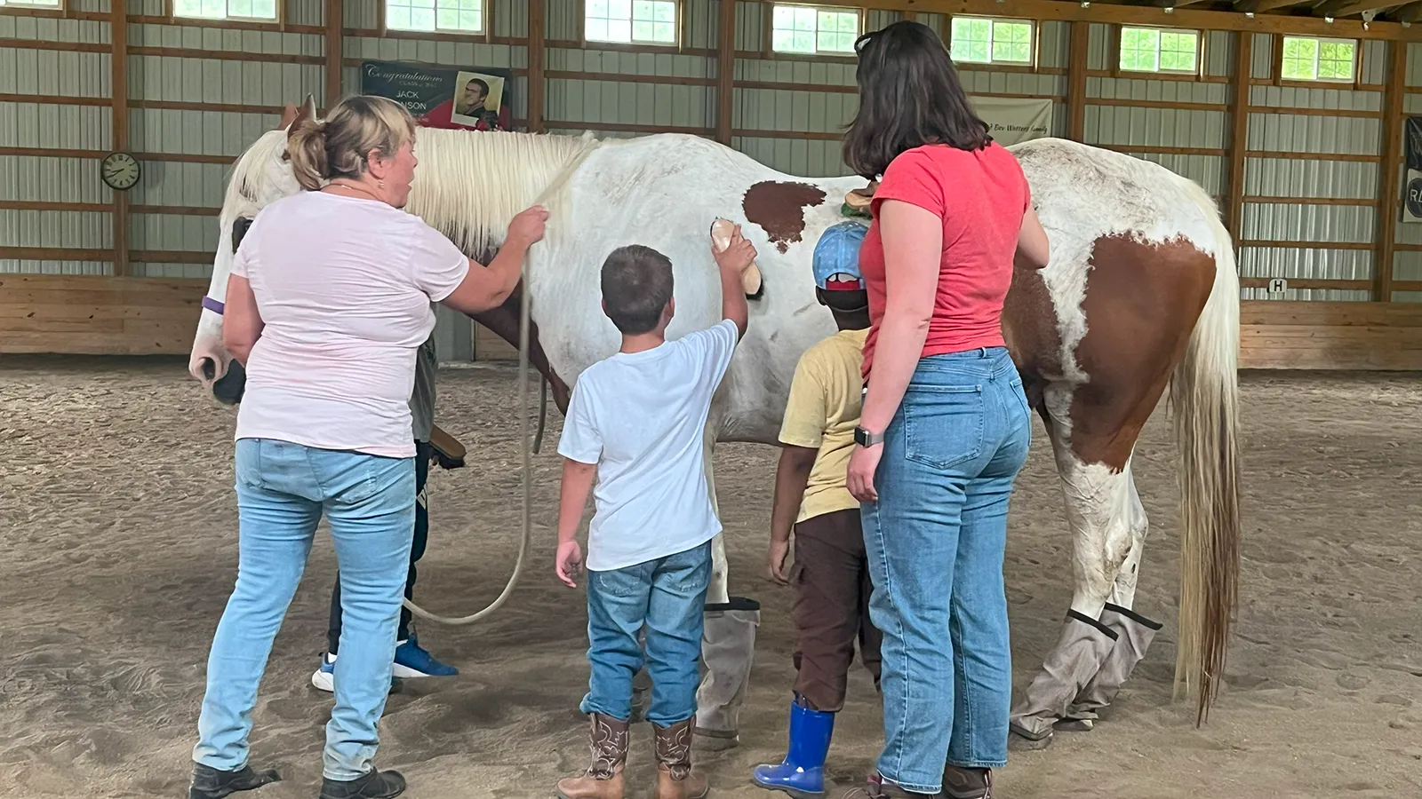 2 adults and 2 children brushing a horse