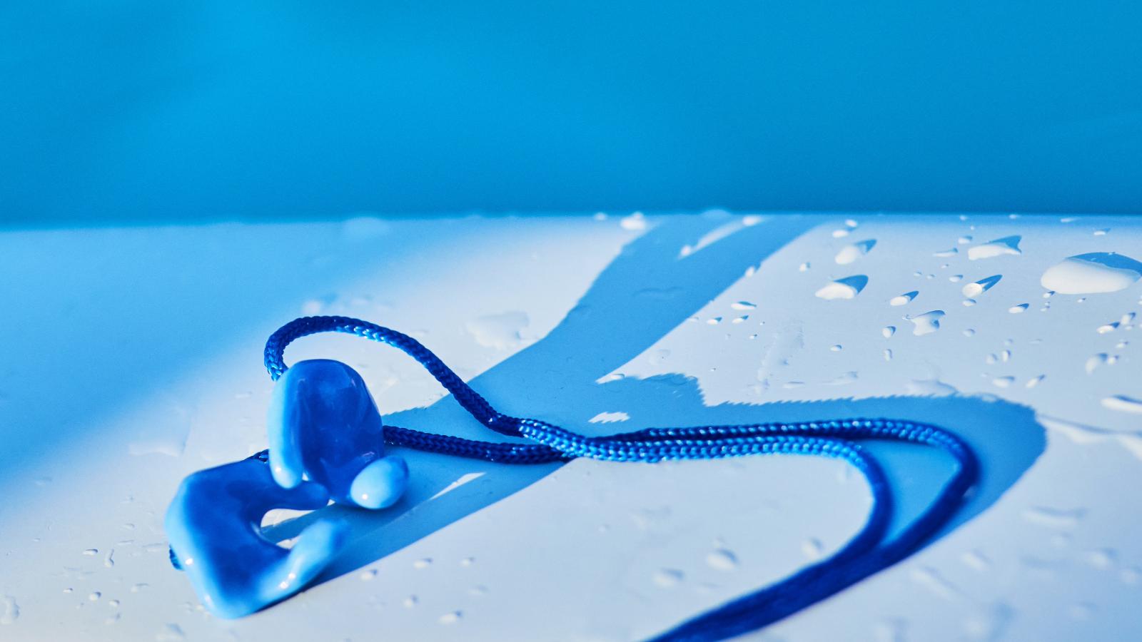 Sleek, molded swimming earplugs rest on a wet surface