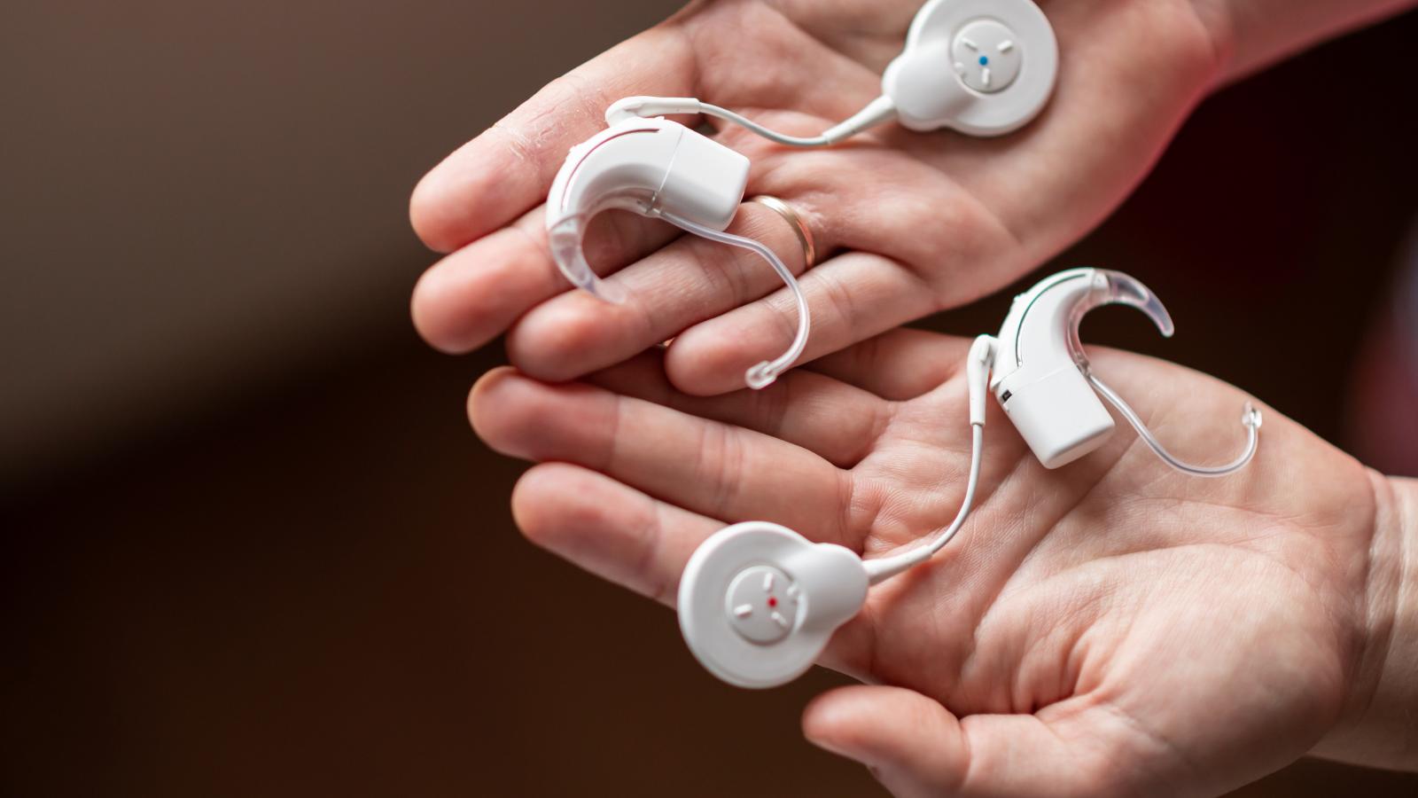Cochlear implant devices resting in open hands. 