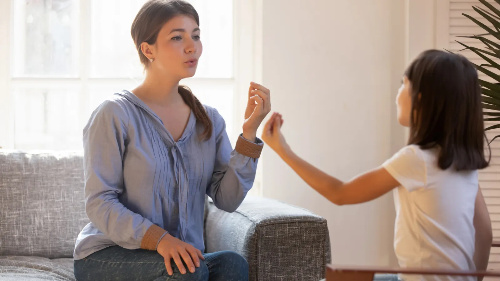 Female speech therapist doing exercise, speaking with little girl patient 