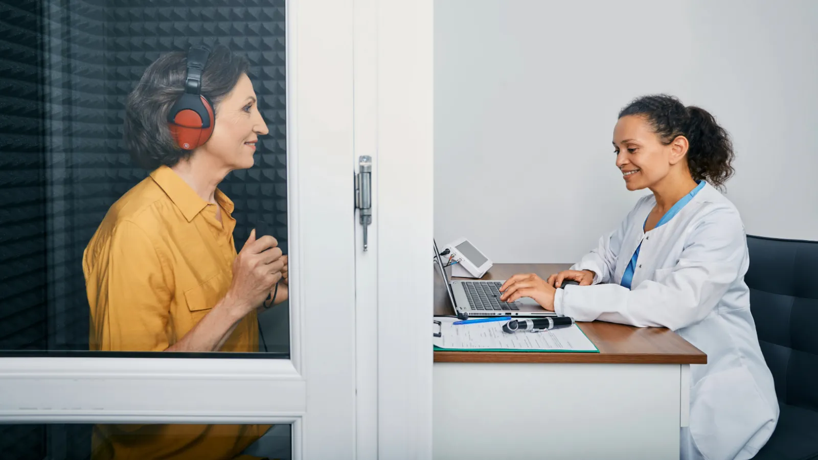 Audiologist doing hearing check-up to a senior citizen woman in soundproof audiometric booth.