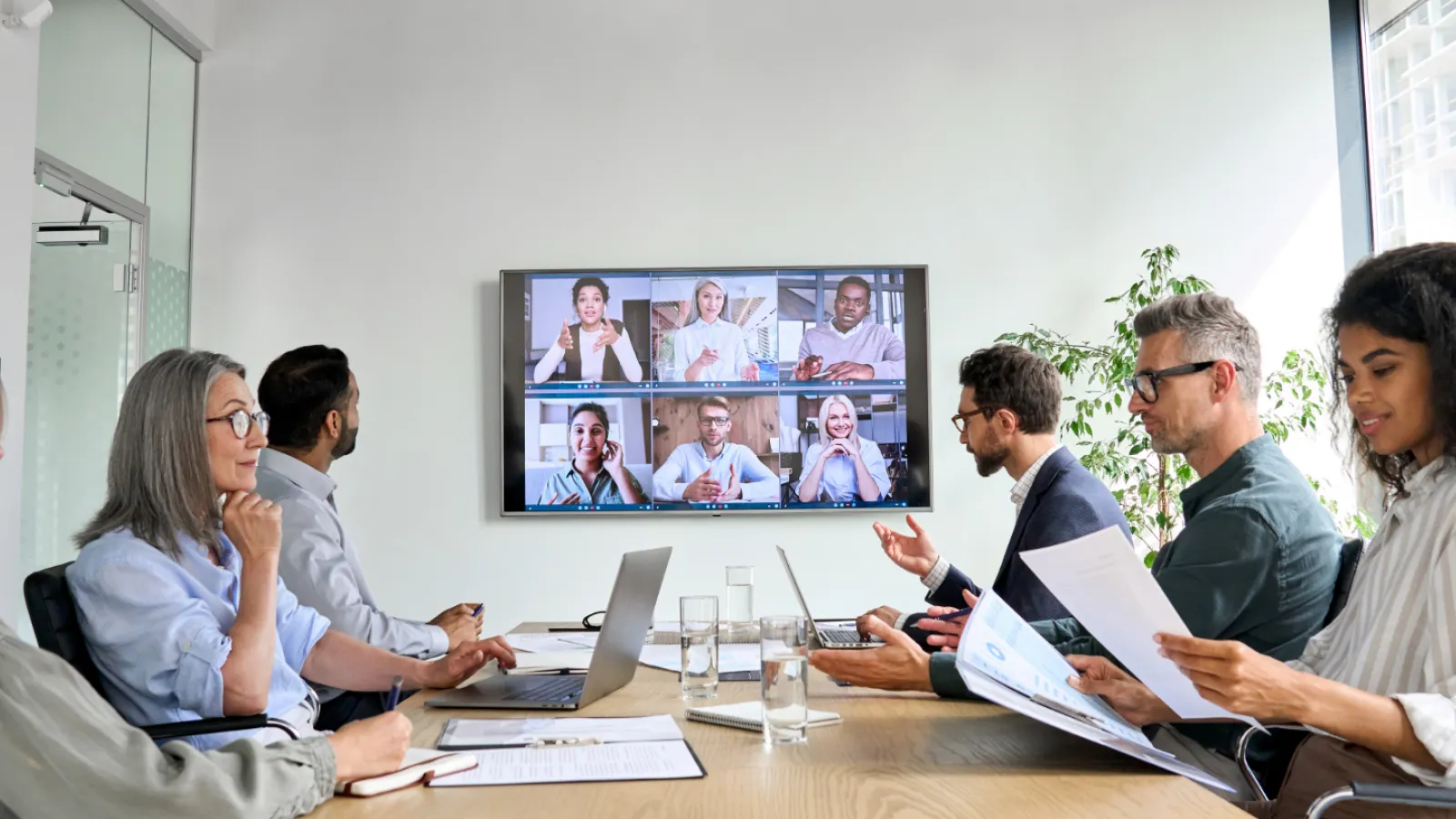 Diverse company employees having online business conference video call on tv screen monitor in board meeting room