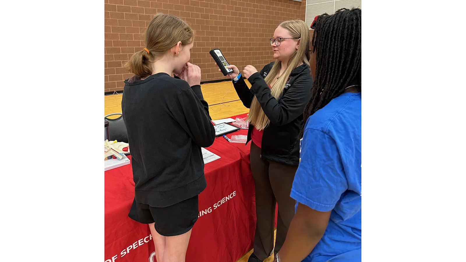 Graduate student demonstrating a device to 2 young people