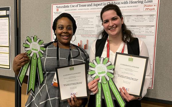 Kristina Bowdrie and Isabella Jamsek posing before research poster with prize ribbons and certificates