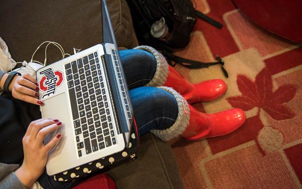 Student typing on laptop with Ohio State sticker and red boots