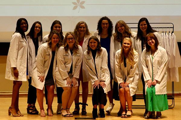 12 AuD students posing in white coats at ceremony
