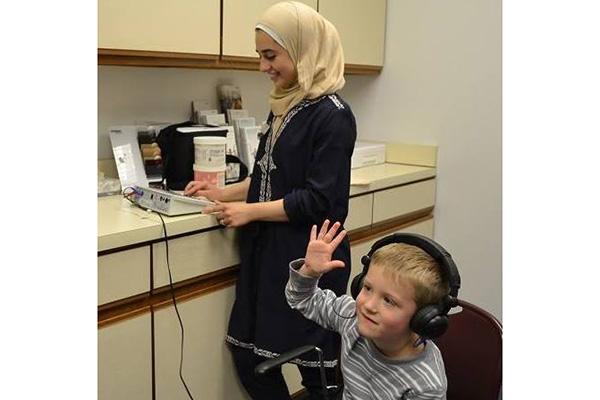 Child with headphones raising hand while student clinician administers hearing test