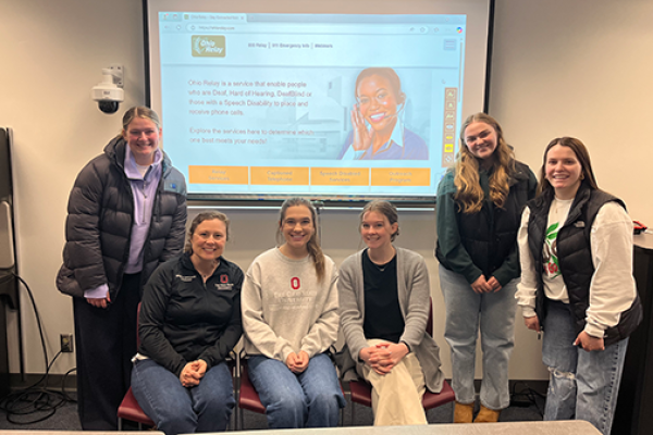 Group photo of students and instructor posing in front of presentation screen