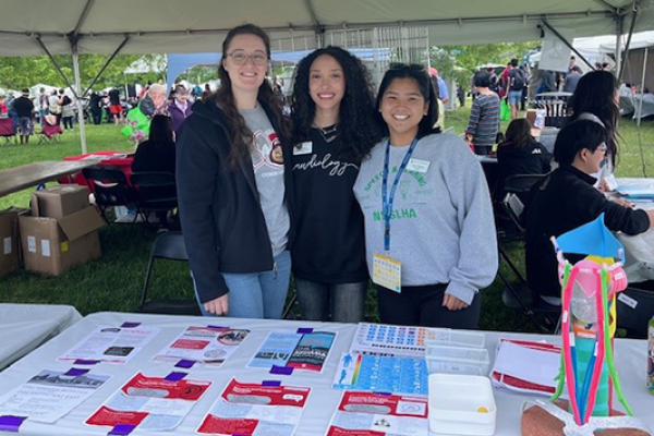 3 students at table under a tent at festival