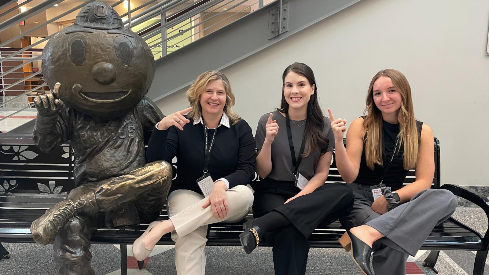 Erika Hagen, Nicole Viola and Courtney Jewell posing beside Brutus sculpture on bench