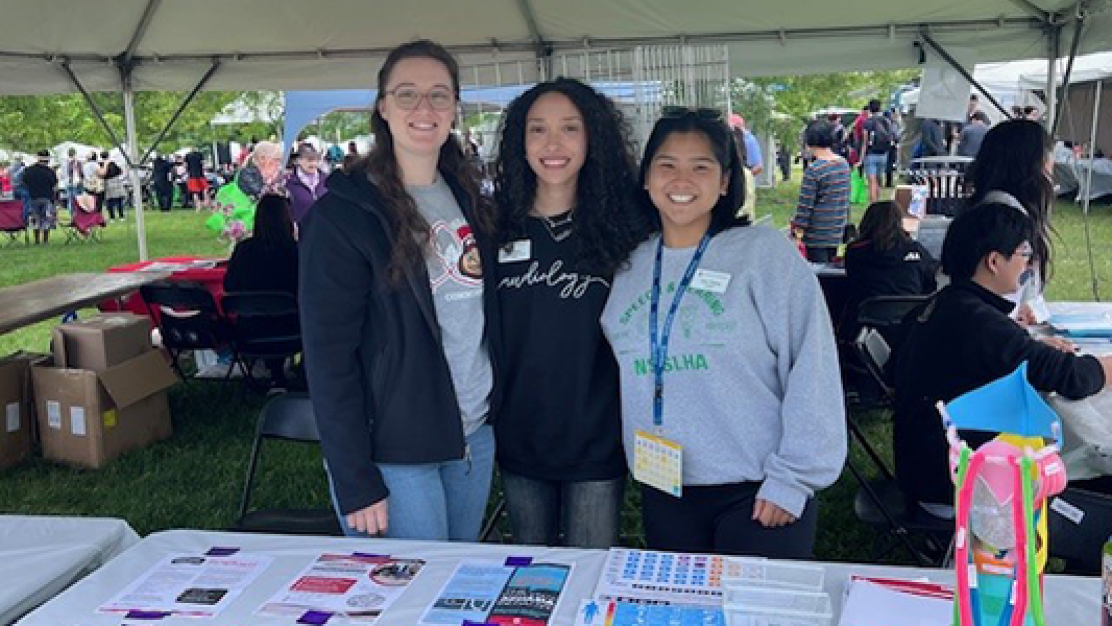 3 students at table under a tent at festival