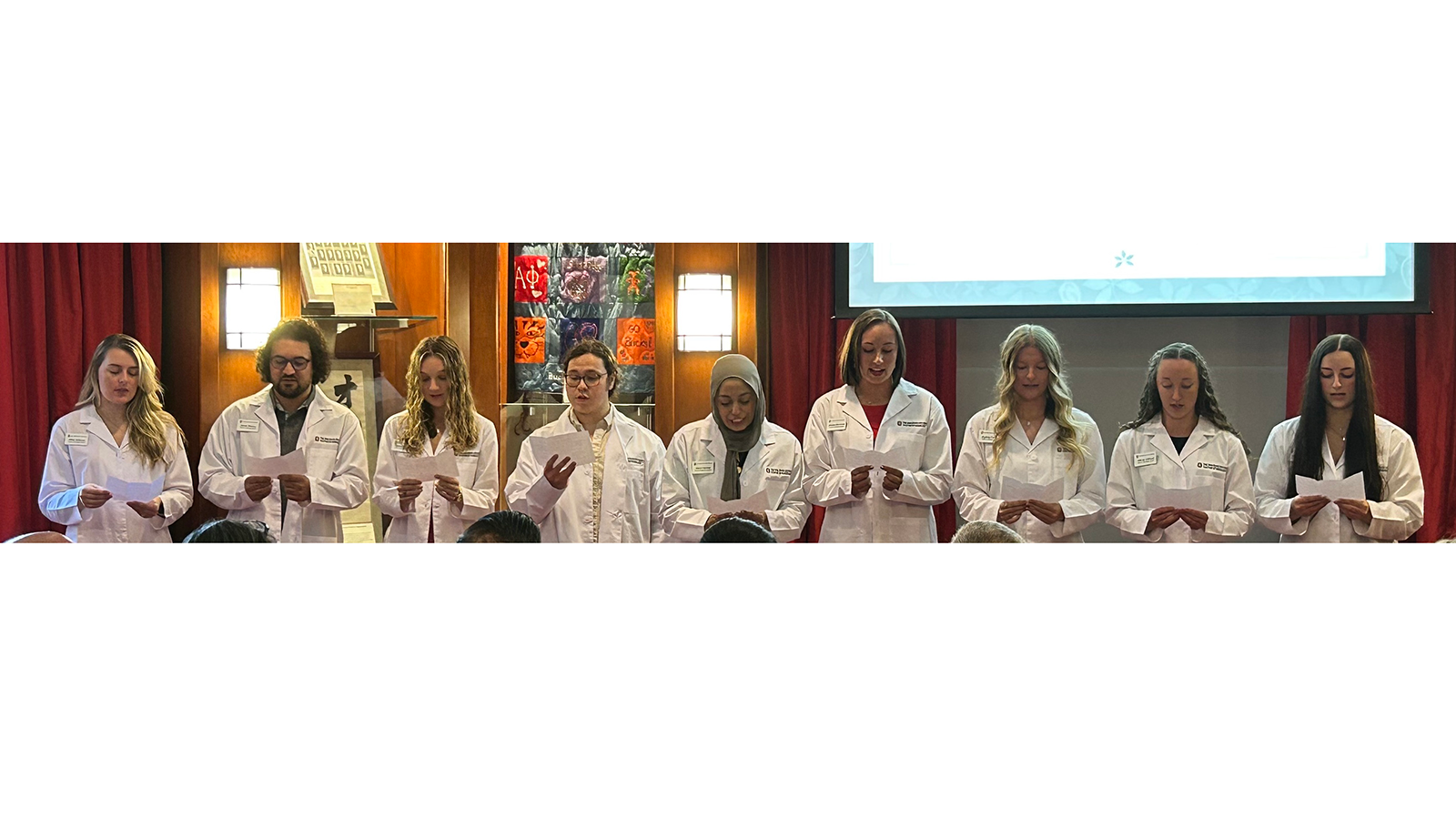 9 students in white coats reciting professional oath